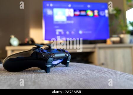 Brecht, Belgique - 31 octobre 2019 : une tournée sur PLAYSTATION 4 controller allongé sur un canapé devant la télévision affichant le playstation home scre Banque D'Images