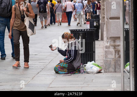 Dame à genoux sur une rue de Venise dans une zone de shopping touristique, qui fait signe à la mendicité cup. De nombreuses personnes ignorent totalement son passé de marche. Banque D'Images