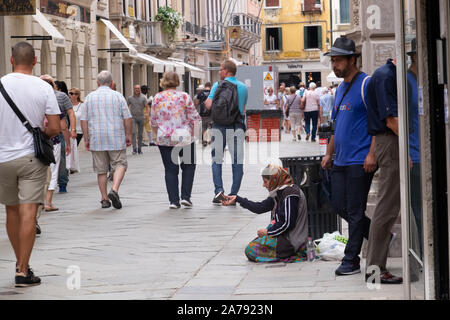 Dame à genoux sur une rue de Venise dans une zone de shopping touristique, qui fait signe à la mendicité cup. De nombreuses personnes ignorent totalement son passé de marche. Banque D'Images