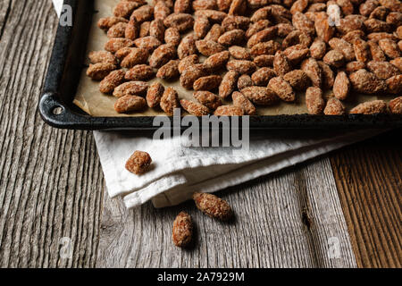 Amandes brûlées étendu sur la lèchefrite, noir, papier chiffon blanc texturé rustique sur table en bois, l'accent sur trois amandes brûlées dans l'avant-plan Banque D'Images