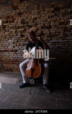 Le violoncelliste solitaire assise seule dans une zone sombre de brique et de pierre d'un tunnel pour l'abri de la rue pour le passage public sur un violoncelle brillant. Banque D'Images