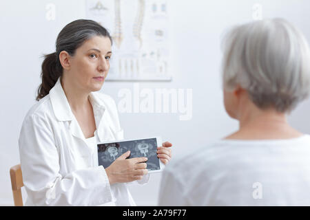 Female doctor with tablet computer montrant son senior patient cat scan images de ses vertèbres dégénérés. Banque D'Images