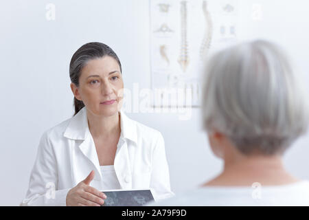 Female doctor with tablet computer montrant son senior patient cat scan images de ses vertèbres dégénérés. Banque D'Images