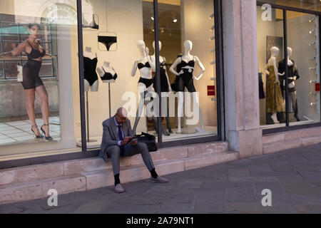 Look de comédie shop homme s'assit sur sill, plongé dans son téléphone tout en tenue légère nuls de la fenêtre Afficher semblent être en train de le regarder avec dégoût. Banque D'Images