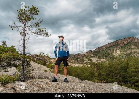 Coureur masculin debout sur un rocher dans les montagnes. Exécute l'athlète dans les montagnes au milieu des rochers. L'homme en maillot bleu et short noir à l'extérieur formation Banque D'Images