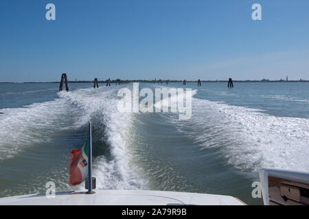 L'accélération de la skyline de Venise dans un bateau-taxi de rabotage , montrant sa vague massive service au soleil, avec le drapeau au premier plan Banque D'Images