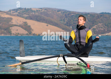 Windsurfer faisant du yoga tout en restant assis sur les planches de surf. Sport et détente concept. Banque D'Images