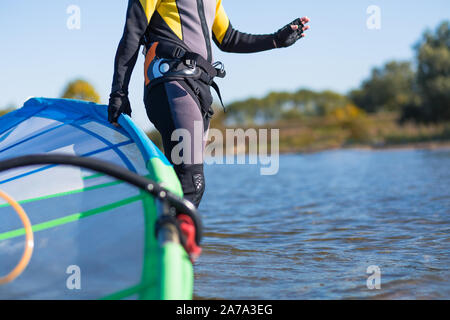 Close up de planche à voile windsurf holding wetsuit en eau peu profonde. Banque D'Images