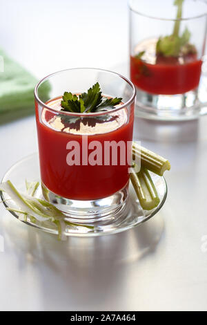 Un verre avec du jus de tomate et le persil décoration, un deuxième verre de jus de tomate et le céleri branche. Banque D'Images