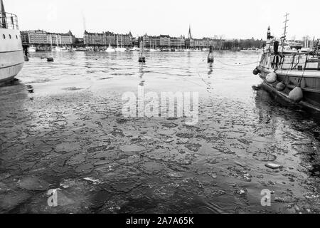 Image en noir et blanc de la rivière au centre-ville de Stockholm port avec deux bateaux sur les côtés, de l'eau glacée à l'avant-plan et la vieille ville dans la zone Banque D'Images