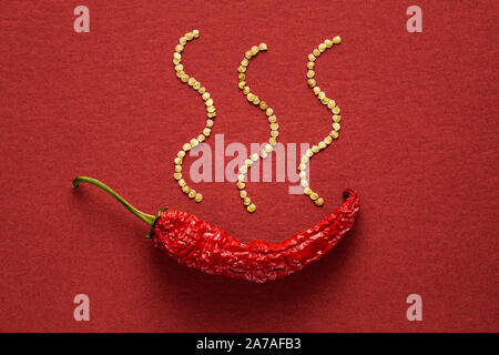 Seul le poivre rouge banane séchée sur un fond de papier rouge avec des graines de poivre Banque D'Images