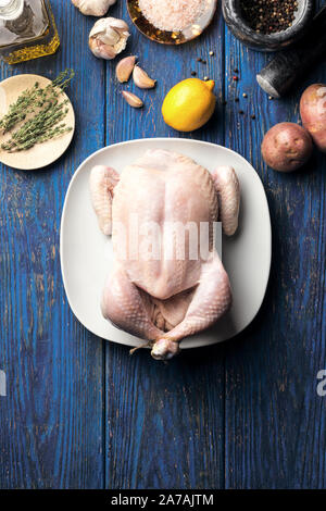 Le poulet cru dans une assiette blanche sur un fond en bois bleu avec le citron et le thym, et divers ingrédients, mise à plat Banque D'Images