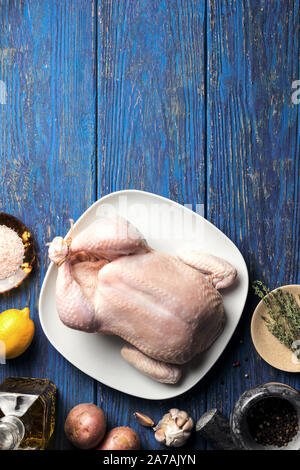 Le poulet cru dans une assiette blanche sur un fond en bois bleu avec le citron et le thym, et divers ingrédients, mise à plat Banque D'Images