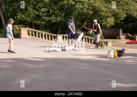 Girl lying on floor pour prendre une photo d'un chien alors que l'homme détient le matériel d'éclairage et un autre chien tient en laisse. Une autre fille attention chiens dessin Banque D'Images