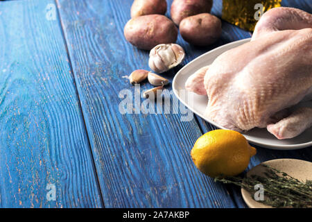 Le poulet cru dans une assiette blanche sur un fond en bois bleu avec le citron et le thym, et divers ingrédients, side view Banque D'Images