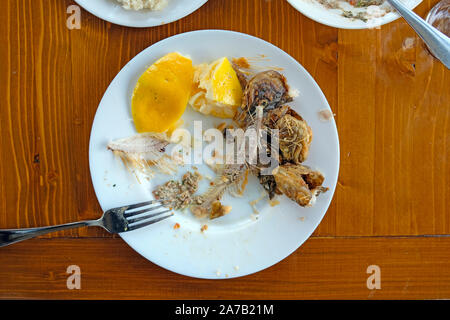 Sur une plaque blanche sont des os d'un mangé du poisson frit et des tranches de citron. Sur une table en bois brun est une plaque blanche avec une fourchette et restes de nourriture Banque D'Images