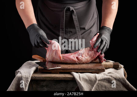 Gants en latex noir en chef tient un lapin entier sur une carcasse brown à découper, processus de la cuisson des viandes Banque D'Images