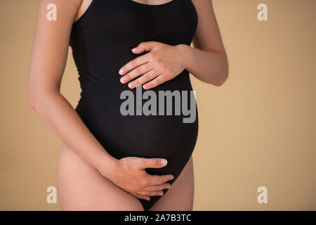 Ventre enceinte close up. Fille enceinte dans un élégant body noir. Belle grossesse en santé. Le minimalisme Banque D'Images