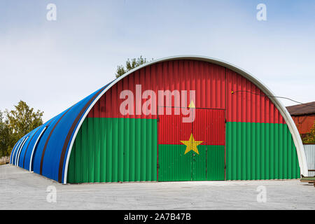 Close-up du drapeau national du Burkina Faso peint sur la paroi métallique de l'entrepôt d'un grand territoire fermé contre le ciel bleu. Le concept de sto Banque D'Images