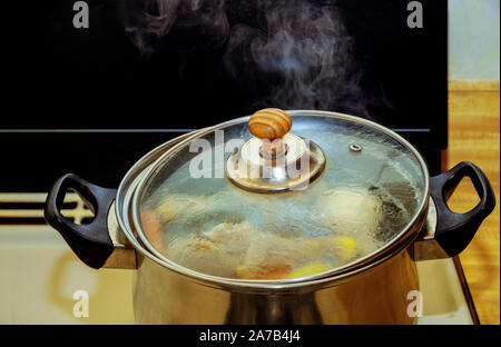 Bouillon de poulet fait maison avec de la viande sur les os et les légumes d'un metal sur cuisinière à gaz Banque D'Images