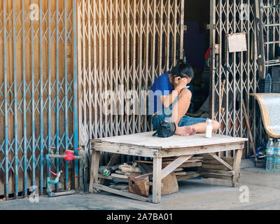 Une femme d'âge moyen est assis et en tirant ses cheveux gris avec des pincettes et un miroir d'elle-même devant sa maison pendant son temps libre. Banque D'Images