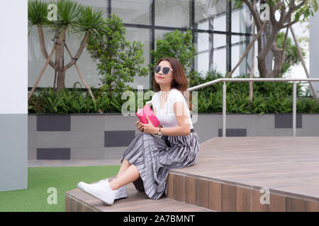 Happy young woman wearing sunglasses assis sur des escaliers et de l'écriture à l'extérieur de l'ordinateur portable. Banque D'Images