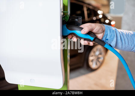 Homme de brancher le câble dans la station de recharge pour voitures électriques à la concession automobile, close-up view Banque D'Images