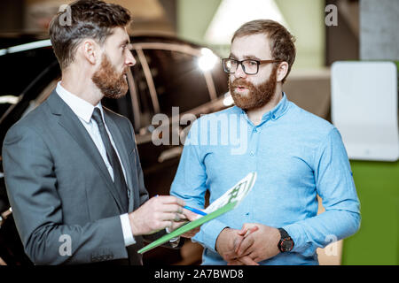 Sales consultant à parler avec un client, qui traite certaines choses formelle à l'agence de voiture. Concept de l'achat de voitures électriques Banque D'Images