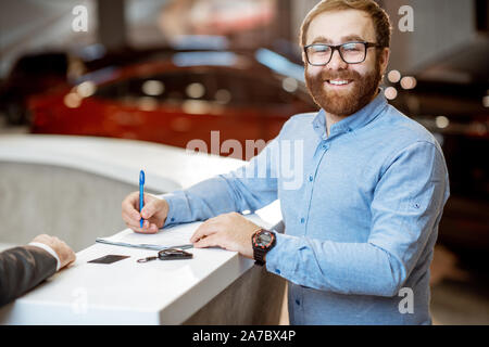 Portrait d'un jeune homme comme un heureux acheteur de signer certains documents, l'achat d'une voiture dans la showroom moderne de la voiture Banque D'Images