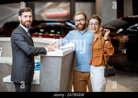 Portrait d'un directeur des ventes en serrant la main d'un heureux acheteurs à l'agence de voiture. Jeune couple d'achat de nouvelles voiture électrique Banque D'Images