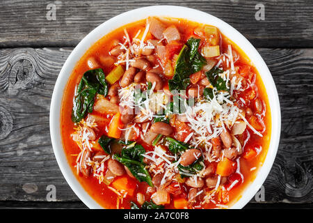 Close-up of italian borlotti ou haricots canneberges soupe avec des légumes, céleri, épinards, parmesan et tomates dans un bol blanc sur une table en bois rustique, Banque D'Images