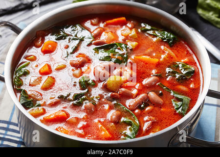 Close-up of italian borlotti ou haricots canneberges soupe avec des légumes, céleri, épinards, parmesan et tomates dans une casserole de métal sur un onglet en bois noir Banque D'Images