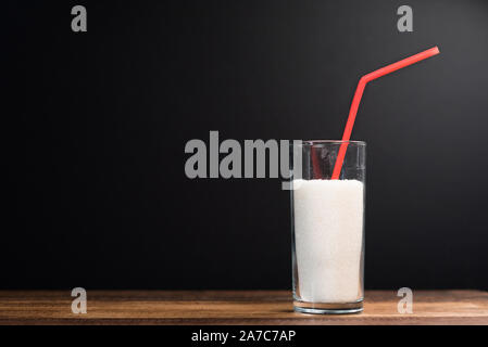 Un verre plein de sucre blanc avec de la paille sur fond noir. Concept de la mauvaise alimentation et diabète Banque D'Images