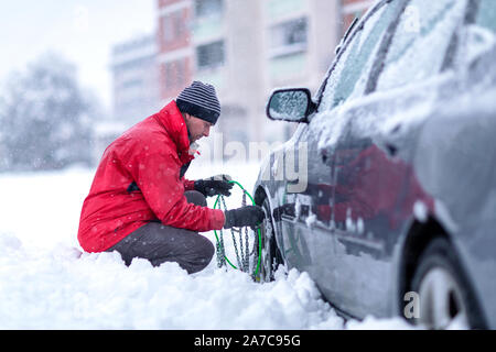 Jeune homme de mettre sur les chaînes d'hiver car.confondu l'homme ne sait pas comment mettre des chaînes à neige sur pneu de voiture. Banque D'Images