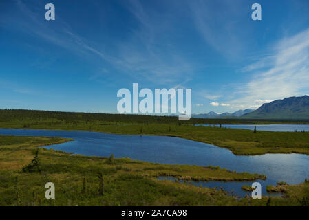 Vue depuis une voiture en mouvement sur la Glenn Highway près du col de Tahneta jusqu'à un lac sur le plateau et les montagnes de Chugach en arrière-plan. Banque D'Images