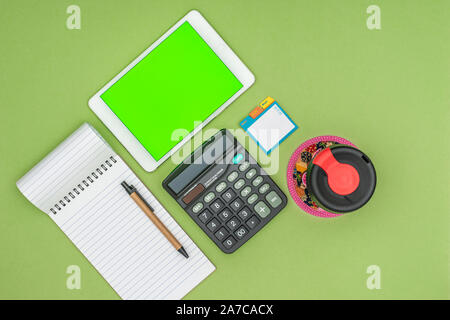 Tablette écran vert, de fournitures scolaires, la tasse de café réutilisable sur fond vert. Mise à plat de haut en bas. Technologie concept de Business Objects. Banque D'Images