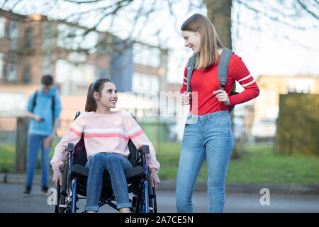 Teenage Girl In Wheelchair Talking With Friend comme ils quittent l'école secondaire Banque D'Images