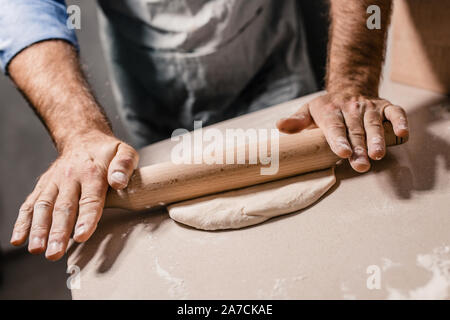 Les mains d'un boulanger avec un rouleau à pâtisserie en bois fait rouler la pâte en une fine couche sur la table Banque D'Images