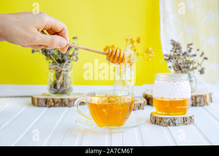 Tasse de thé en verre avec linden en herbes organiques naturelles et un pot de miel sur une table en bois blanc. Augmenter l'immunité dans la saison fraîche. Banque D'Images