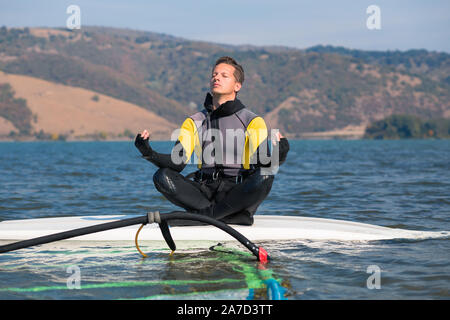 Windsurfer faisant du yoga tout en restant assis sur les planches de surf. Sport et détente concept. Banque D'Images