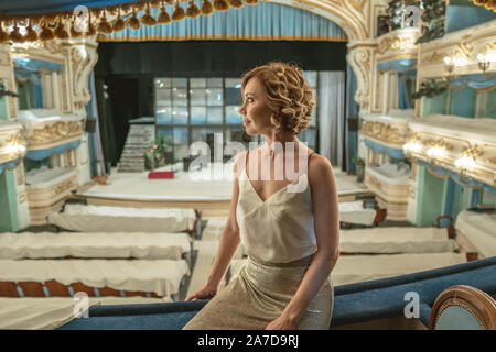 Une belle femme dans une robe seule sur le balcon d'un théâtre vide classique porte sur la scène et de l'intérieur Banque D'Images