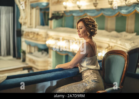 Une belle femme dans une robe seule sur le balcon d'un théâtre vide classique porte sur la scène et de l'intérieur Banque D'Images