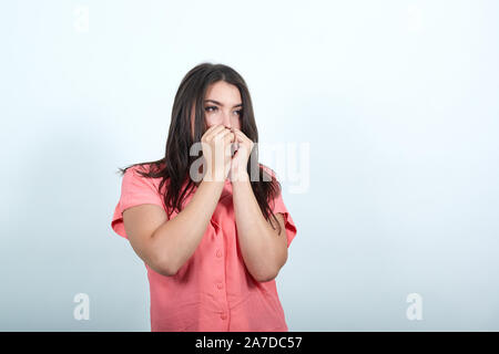 Femme de plus de mur blanc est un peu nerveux et effrayé, mettant les mains à la bouche. Banque D'Images