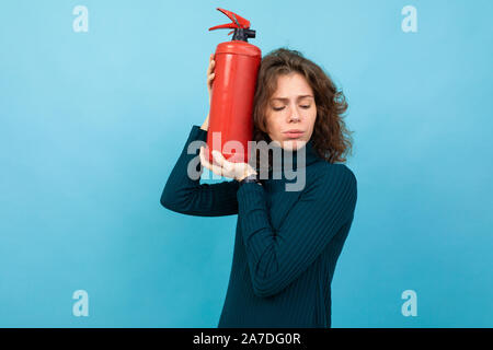 Jeune et belle fille de race blanche avec des cheveux bouclés keepsfire extincteur, portrait isolé sur fond bleu Banque D'Images