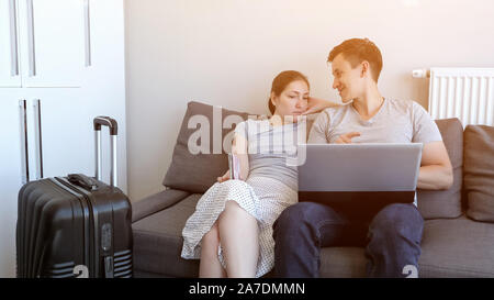 Jeune couple est réservation transfert à l'aéroport sur laptop sitting on sofa at home. Ils vont en vacances avec les passeports et les bagages. Le choix et la réservation d' et l'hôtel. Banque D'Images