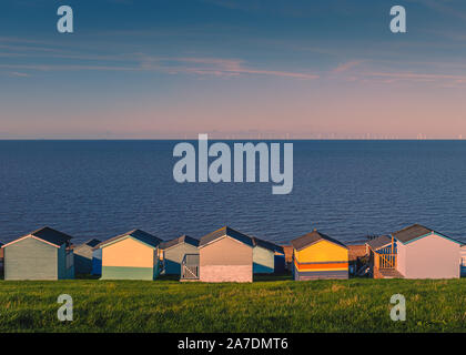 Cabines colorées le long d'un bord à l'herbe, Tankerton Whitstable, Kent, UK. La mer et le ciel sont bleus sur une journée d'hiver ensoleillée, tard dans l'après-midi. E Banque D'Images