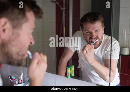 Homme nettoyer les dents le matin salle de bains à la maison, en regardant le miroir. Soins d'hygiène quotidienne Banque D'Images