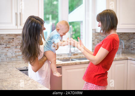 La notion de maternité, nanny, la petite enfance et l'enfance. Une balle dans la cuisine. Deux femmes et un bébé dans leurs bras, une famille heureuse Banque D'Images