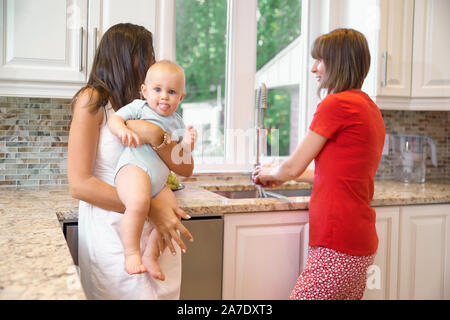 La notion de maternité, nanny, la petite enfance et l'enfance. Une balle dans la cuisine. Deux femmes et un bébé dans leurs bras, à la recherche dans l'appareil photo et s Banque D'Images