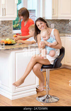 La notion de maternité, nanny, la petite enfance et l'enfance. Une balle dans la cuisine. Deux femmes et un bébé dans leurs bras, à la recherche dans l'appareil photo et s Banque D'Images